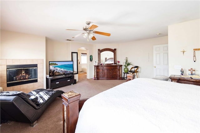 bedroom featuring a tiled fireplace, ceiling fan, and carpet