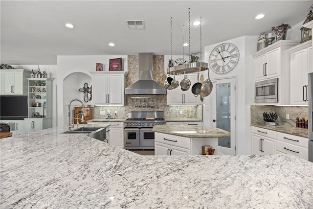 kitchen featuring a large island, light stone counters, tasteful backsplash, wall chimney exhaust hood, and stainless steel appliances