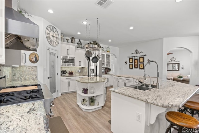 kitchen featuring appliances with stainless steel finishes, decorative backsplash, white cabinetry, a center island with sink, and extractor fan