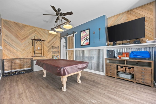 rec room with wood-type flooring, a barn door, wooden walls, billiards, and ceiling fan