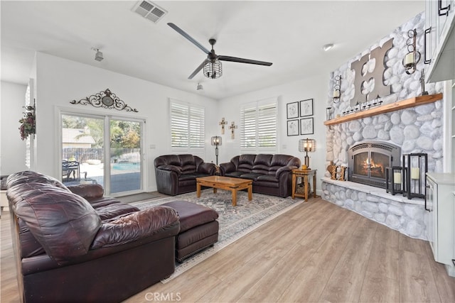 living room with light hardwood / wood-style floors, ceiling fan, and a stone fireplace