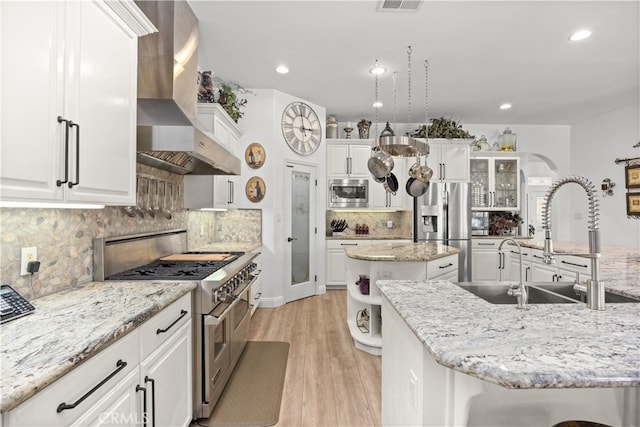 kitchen with white cabinets, appliances with stainless steel finishes, wall chimney exhaust hood, and an island with sink