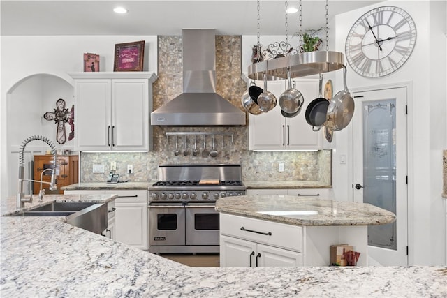 kitchen featuring backsplash, white cabinets, wall chimney range hood, and range with two ovens