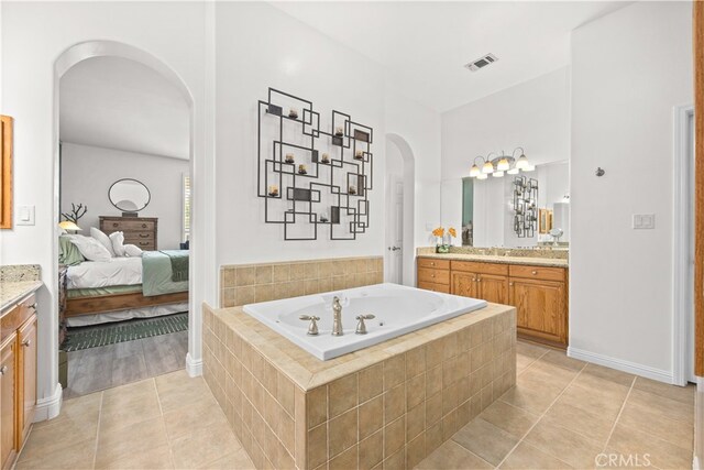 bathroom featuring a relaxing tiled tub, vanity, and tile patterned flooring