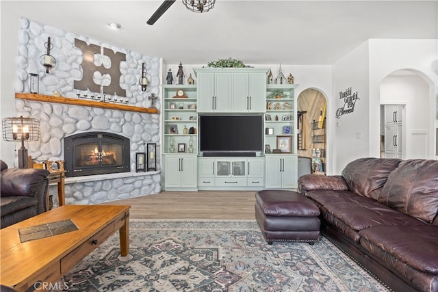 living room featuring ceiling fan, a stone fireplace, and hardwood / wood-style flooring