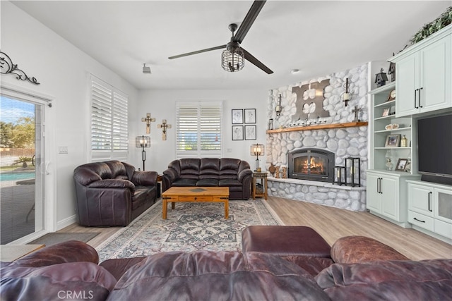 living room featuring light wood-type flooring, a fireplace, ceiling fan, and plenty of natural light