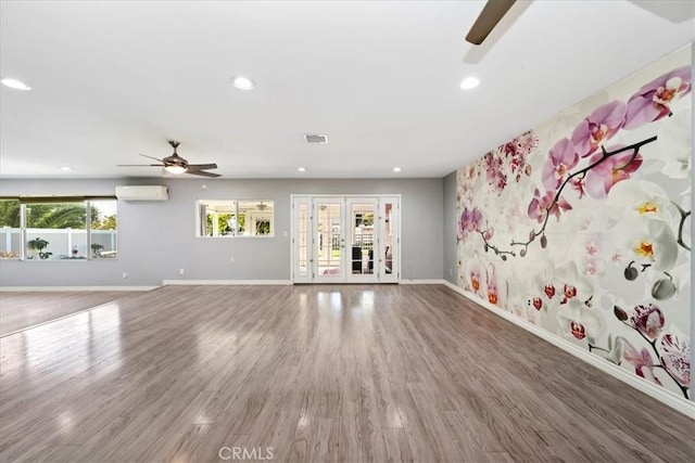 unfurnished living room featuring a wall unit AC, ceiling fan, french doors, and wood-type flooring