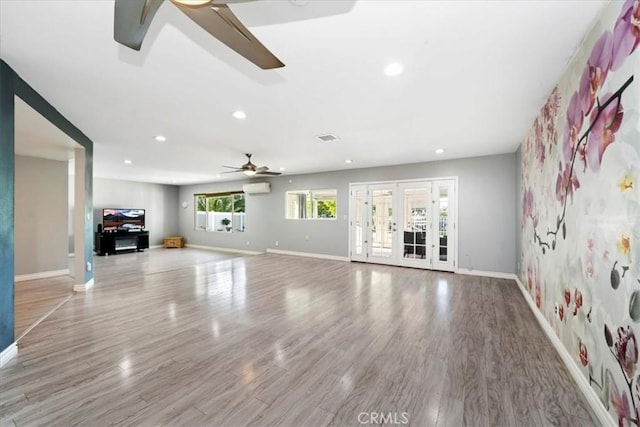 unfurnished living room featuring ceiling fan, light hardwood / wood-style floors, a wall mounted AC, and french doors