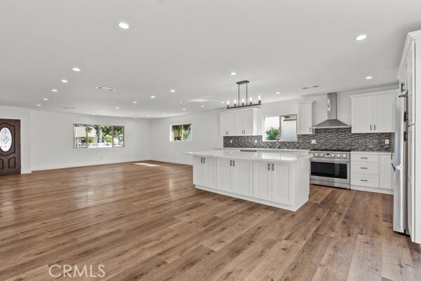 kitchen with wall chimney exhaust hood, light hardwood / wood-style flooring, stainless steel appliances, and a wealth of natural light