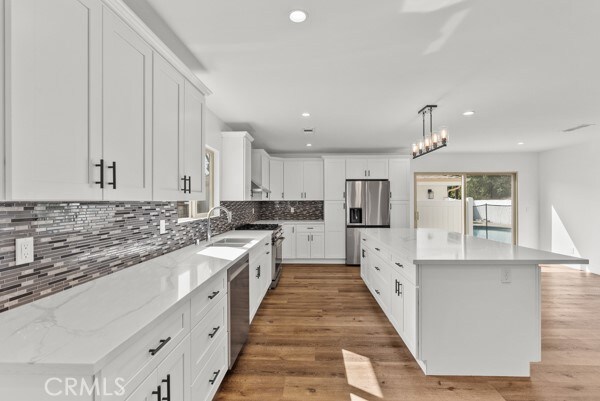 kitchen featuring white cabinets, a kitchen island, appliances with stainless steel finishes, hardwood / wood-style flooring, and decorative light fixtures