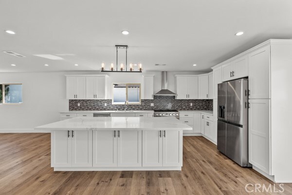 kitchen featuring wall chimney exhaust hood, a center island, appliances with stainless steel finishes, and light hardwood / wood-style floors