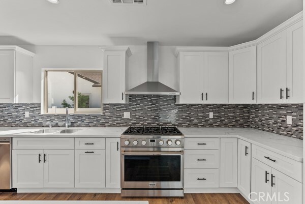 kitchen featuring white cabinetry, wall chimney range hood, stainless steel appliances, and tasteful backsplash