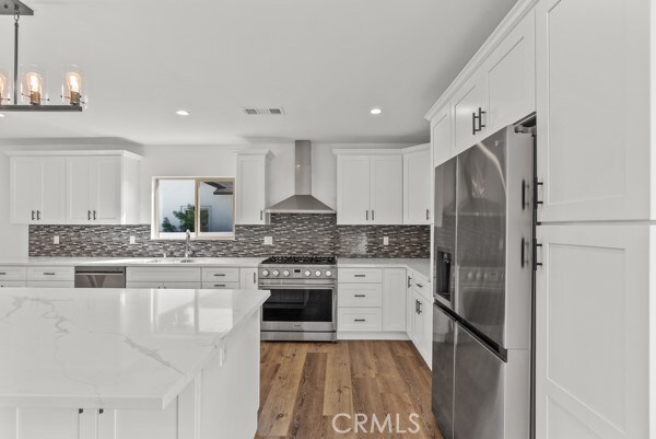 kitchen with hanging light fixtures, appliances with stainless steel finishes, white cabinetry, wall chimney exhaust hood, and light stone counters