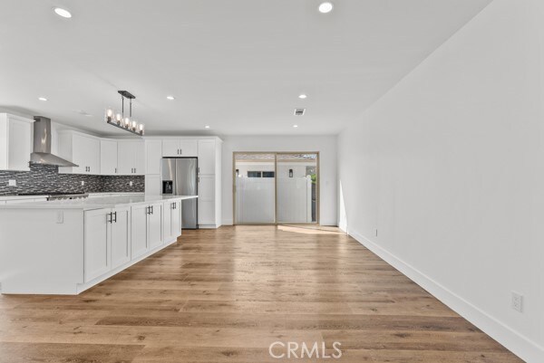 kitchen featuring wall chimney range hood, light hardwood / wood-style flooring, stainless steel refrigerator with ice dispenser, backsplash, and white cabinetry