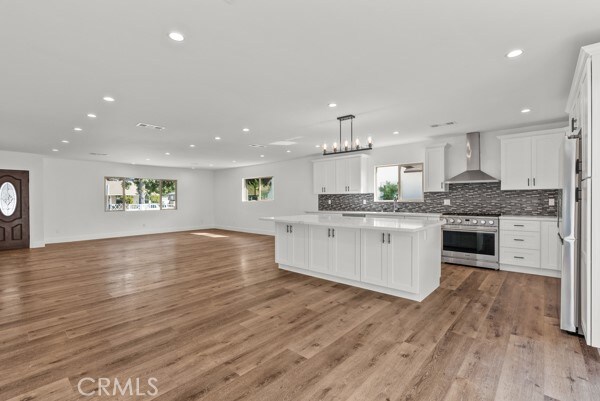 kitchen with a healthy amount of sunlight, stainless steel appliances, wall chimney range hood, and light hardwood / wood-style flooring