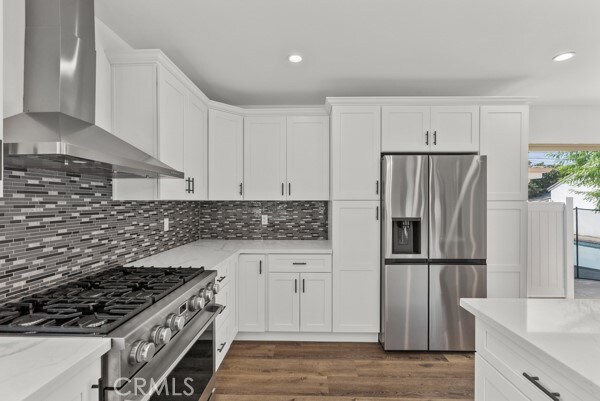 kitchen with tasteful backsplash, wall chimney range hood, white cabinetry, stainless steel appliances, and dark wood-type flooring