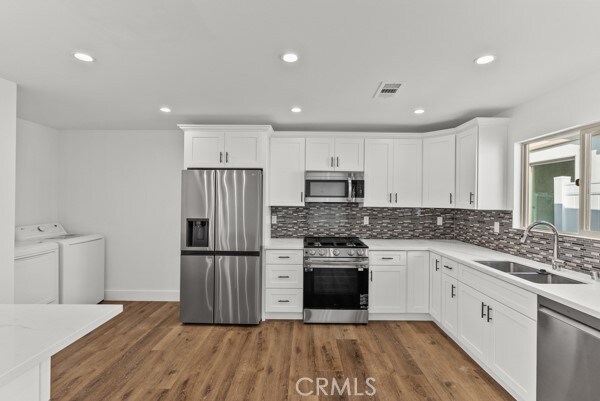 kitchen with sink, washer and dryer, stainless steel appliances, and dark hardwood / wood-style floors