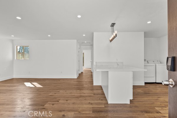 kitchen featuring kitchen peninsula, white cabinets, wood-type flooring, and washer and clothes dryer