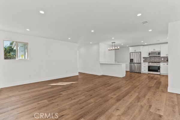 unfurnished living room with an inviting chandelier and light hardwood / wood-style floors