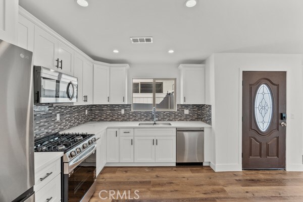 kitchen with dark wood-type flooring, stainless steel appliances, sink, and white cabinets