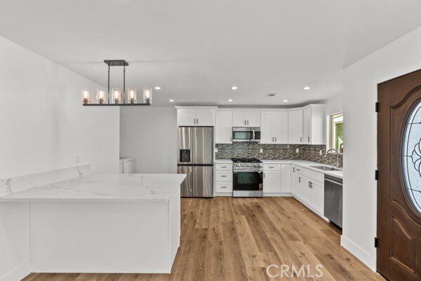 kitchen featuring appliances with stainless steel finishes, kitchen peninsula, pendant lighting, and white cabinets