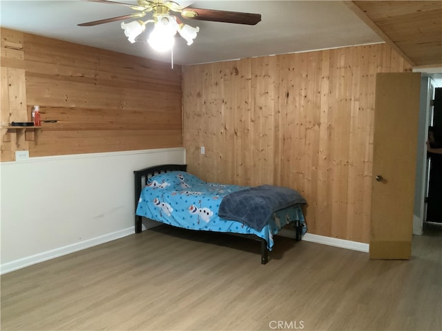 bedroom featuring ceiling fan, hardwood / wood-style flooring, and wood walls