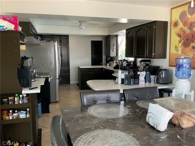 kitchen featuring kitchen peninsula, light tile patterned floors, range hood, ceiling fan, and dark brown cabinetry