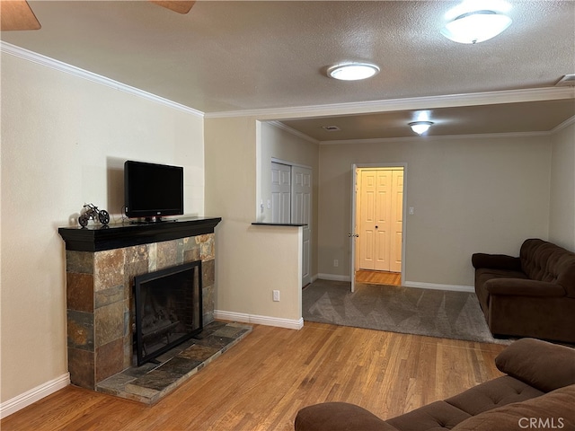 living room with a fireplace, a textured ceiling, wood-type flooring, crown molding, and ceiling fan