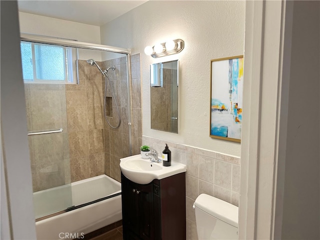 full bathroom with tile walls, vanity, toilet, and bath / shower combo with glass door