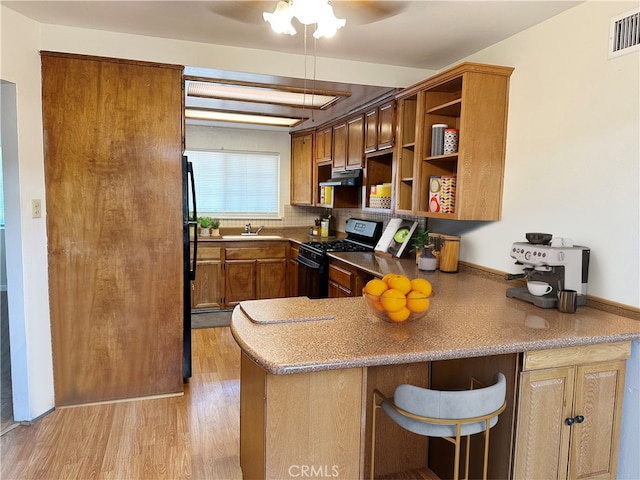 kitchen featuring sink, kitchen peninsula, tasteful backsplash, black appliances, and light hardwood / wood-style floors