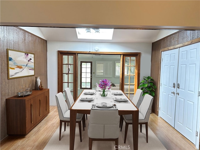 dining space featuring a skylight, light hardwood / wood-style flooring, and wood walls