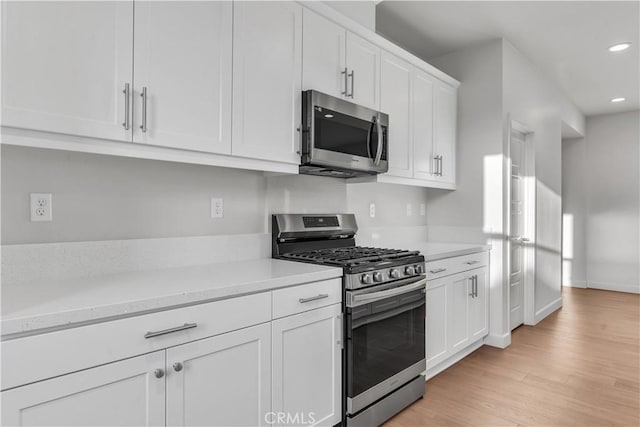 kitchen with light stone countertops, white cabinets, light wood-type flooring, and appliances with stainless steel finishes