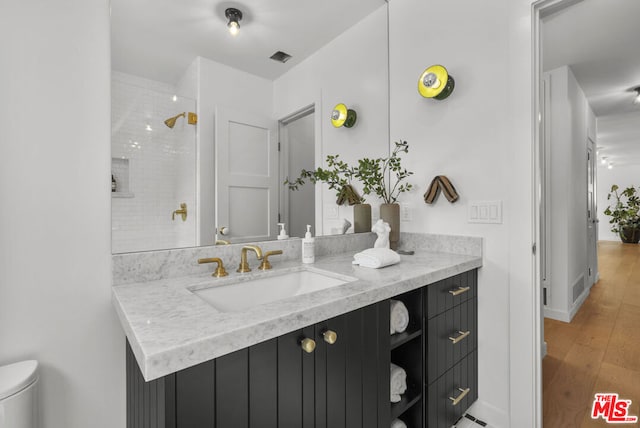 bathroom with a tile shower, hardwood / wood-style floors, vanity, and toilet