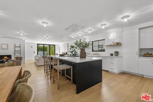 kitchen featuring backsplash, a center island, a breakfast bar area, white cabinetry, and light hardwood / wood-style flooring