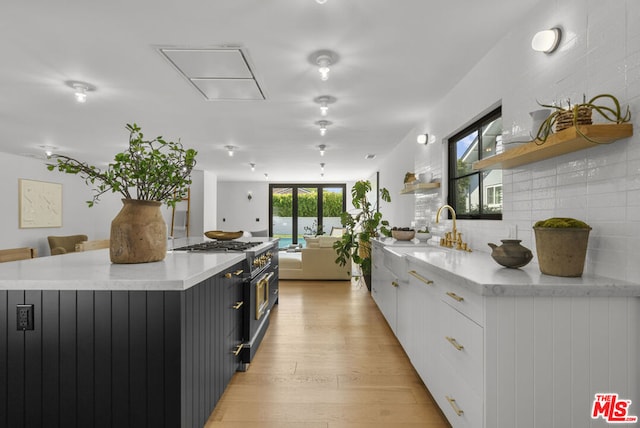 kitchen with white cabinetry, high end range, sink, light hardwood / wood-style floors, and a center island