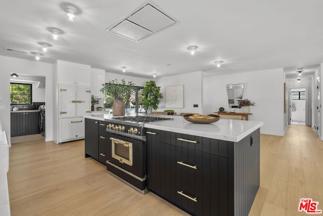 kitchen with a spacious island, white cabinetry, range with two ovens, and light wood-type flooring