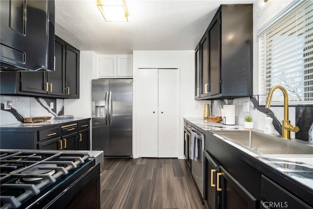 kitchen featuring sink, a textured ceiling, dark wood-type flooring, appliances with stainless steel finishes, and decorative backsplash