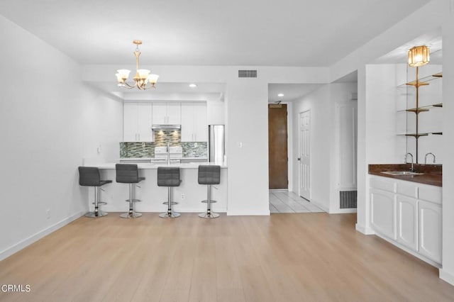 kitchen with white cabinets, a kitchen bar, light hardwood / wood-style floors, and sink