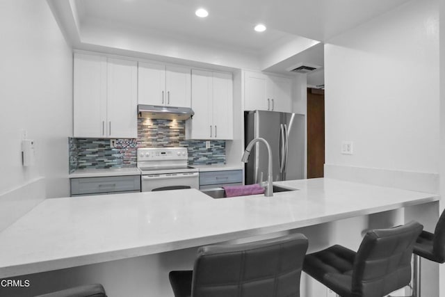 kitchen featuring a breakfast bar, sink, white electric range, white cabinetry, and stainless steel refrigerator