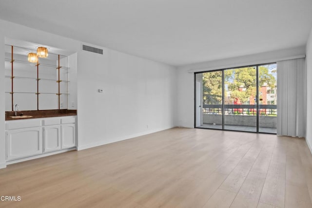 empty room with light hardwood / wood-style floors, a notable chandelier, and sink