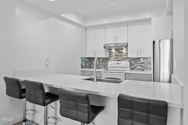 kitchen featuring stainless steel refrigerator, tasteful backsplash, white electric stove, a breakfast bar area, and white cabinets