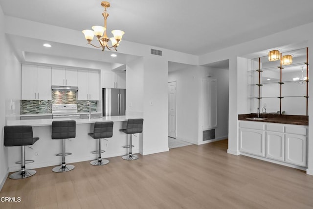 kitchen featuring light hardwood / wood-style flooring, a breakfast bar area, white stove, white cabinetry, and stainless steel refrigerator