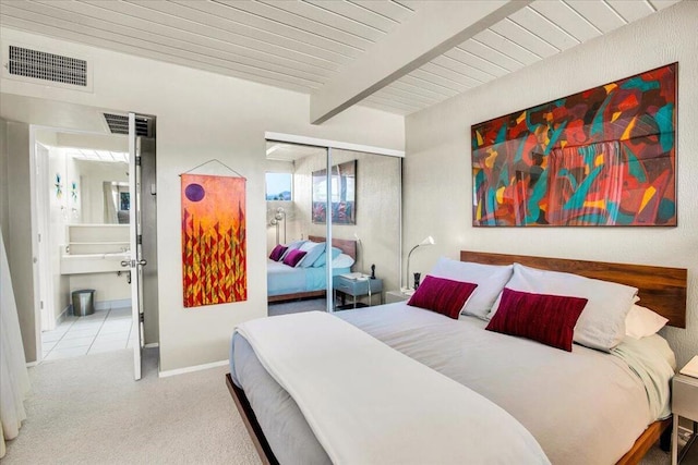 carpeted bedroom featuring beam ceiling and a closet