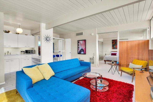 living room with beamed ceiling, light wood-type flooring, and sink