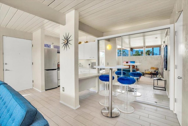 kitchen with sink, beamed ceiling, light hardwood / wood-style floors, white cabinetry, and stainless steel refrigerator