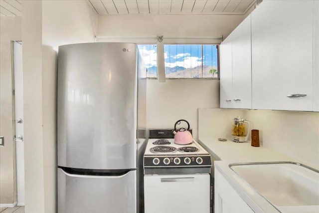 kitchen with stainless steel fridge, electric range, white cabinetry, and sink