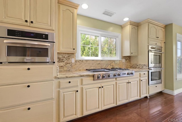 kitchen featuring decorative backsplash, appliances with stainless steel finishes, light stone countertops, cream cabinetry, and dark hardwood / wood-style floors