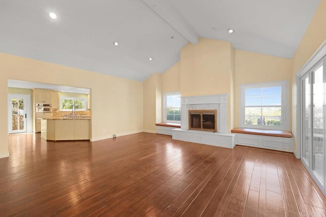 unfurnished living room featuring sink, hardwood / wood-style floors, beamed ceiling, and high vaulted ceiling