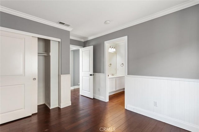 unfurnished bedroom with ensuite bathroom, crown molding, dark wood-type flooring, and a closet