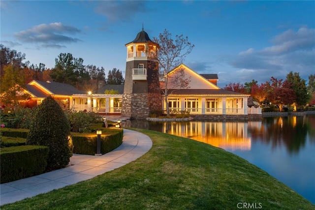 back house at dusk with a yard and a water view